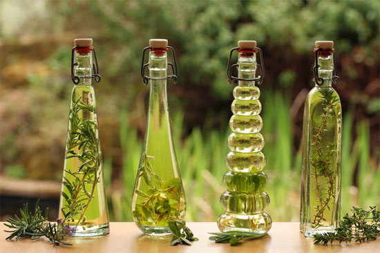 Backlit decorative bottles of herb infused oils with the herbs alongside.
